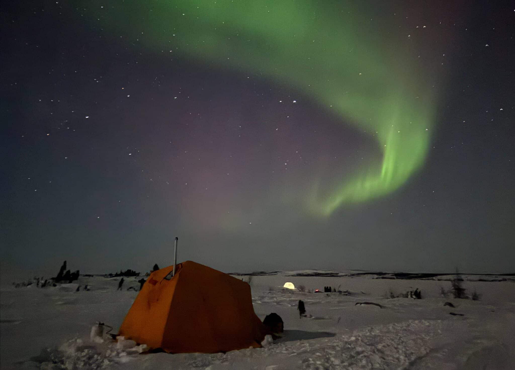 arctic tent in the wild snow surrounded by aurora borealis in the sky